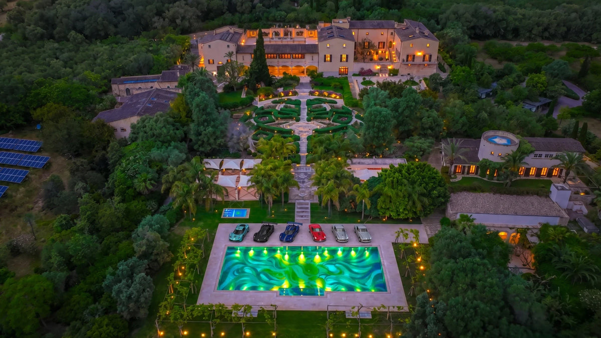 La Casa Principal y sus jardines al anochecer, con la piscina de mosaico iluminada y coches aparcados al lado