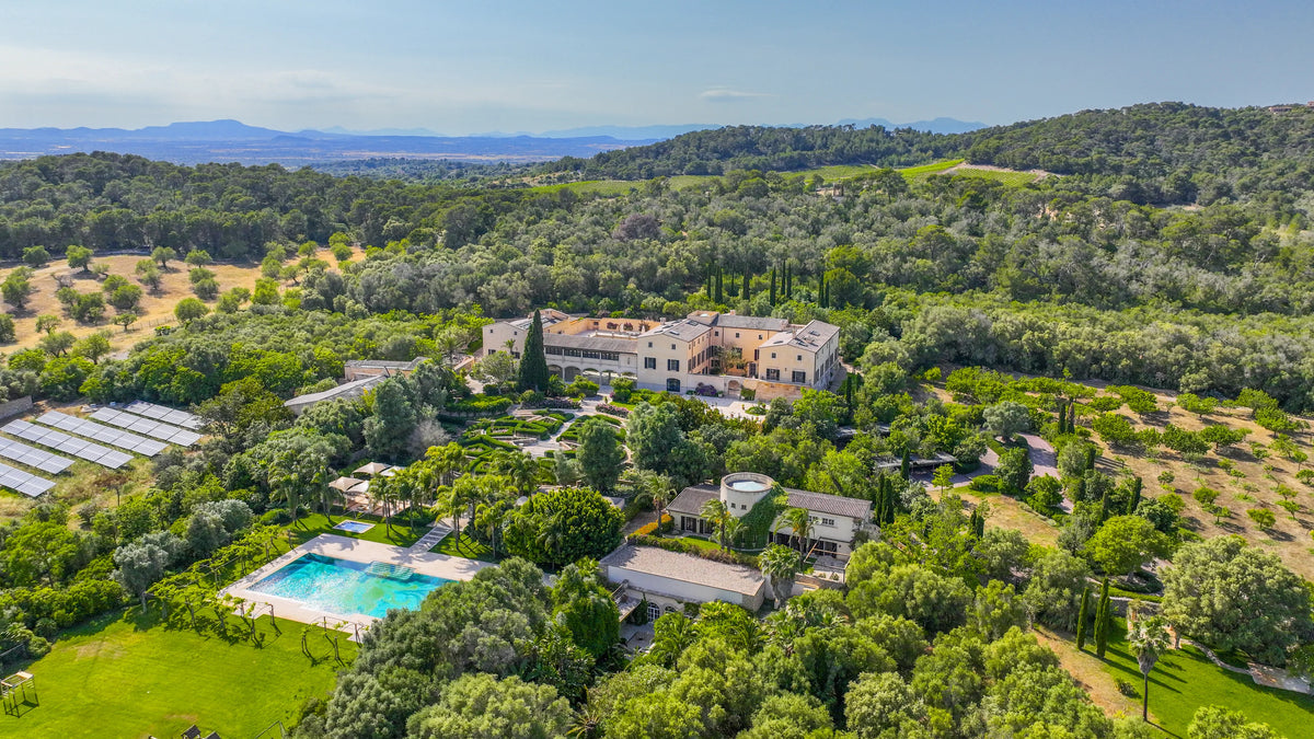 La finca desde el aire: la Casa Principal entre jardines, cipreses y bosques, con el campo hasta las montañas